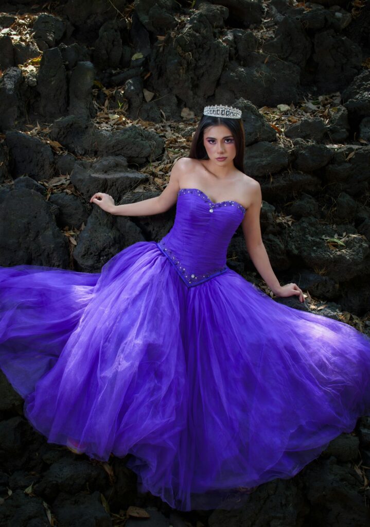 pexels-photo-32542319-32542319 A young woman in a stunning purple gown lies gracefully on dark rocks, exuding elegance and style.